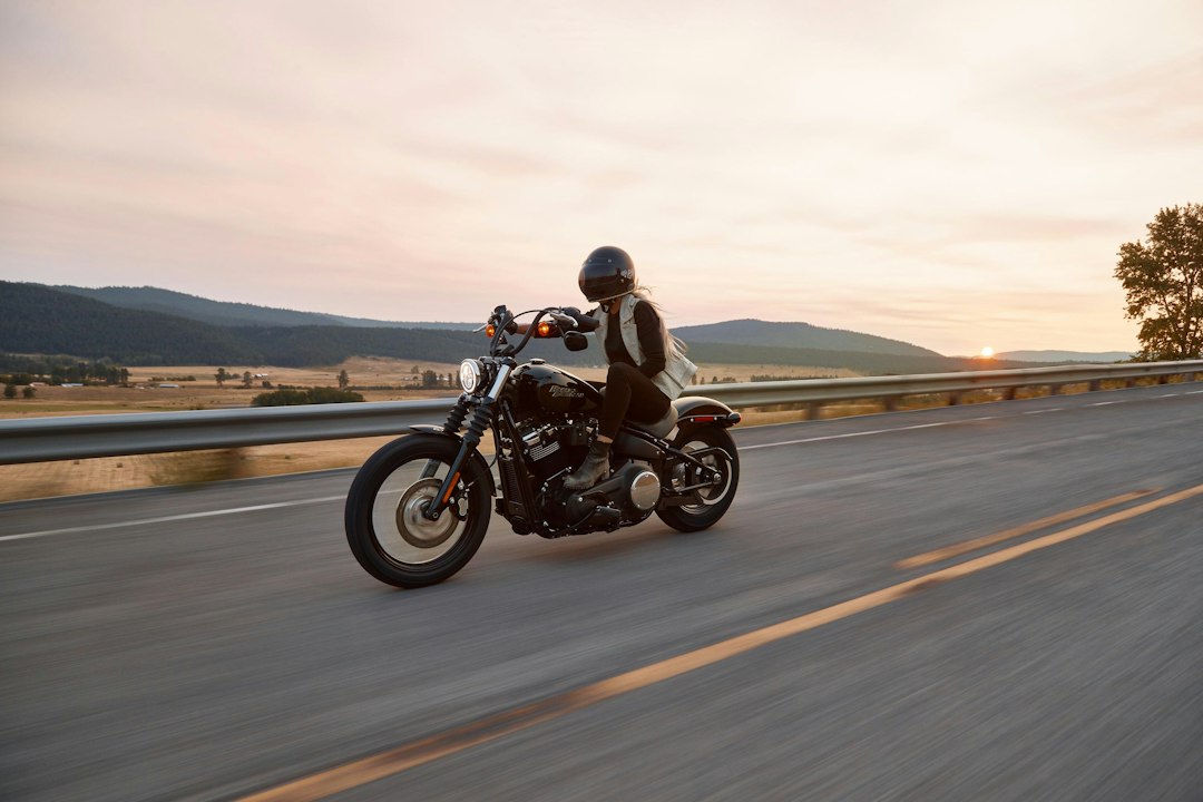 Motociclista pilotando em uma estrada asfaltada ao entardecer com montanhas ao fundo